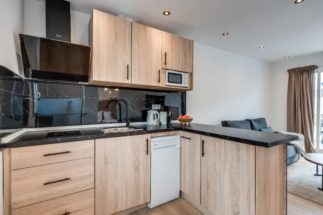 The kitchen: oak cabinets, a dishwasher and a black stone counter, with the terrace doors beyond