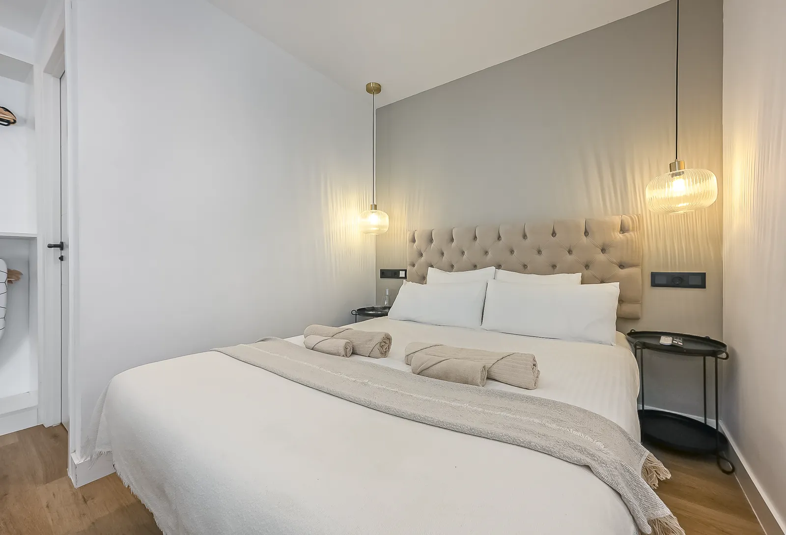 The Signature Suite with Balcony: a double bed with a tufted headboard against a grey wall, a brass pendant hanging on either side