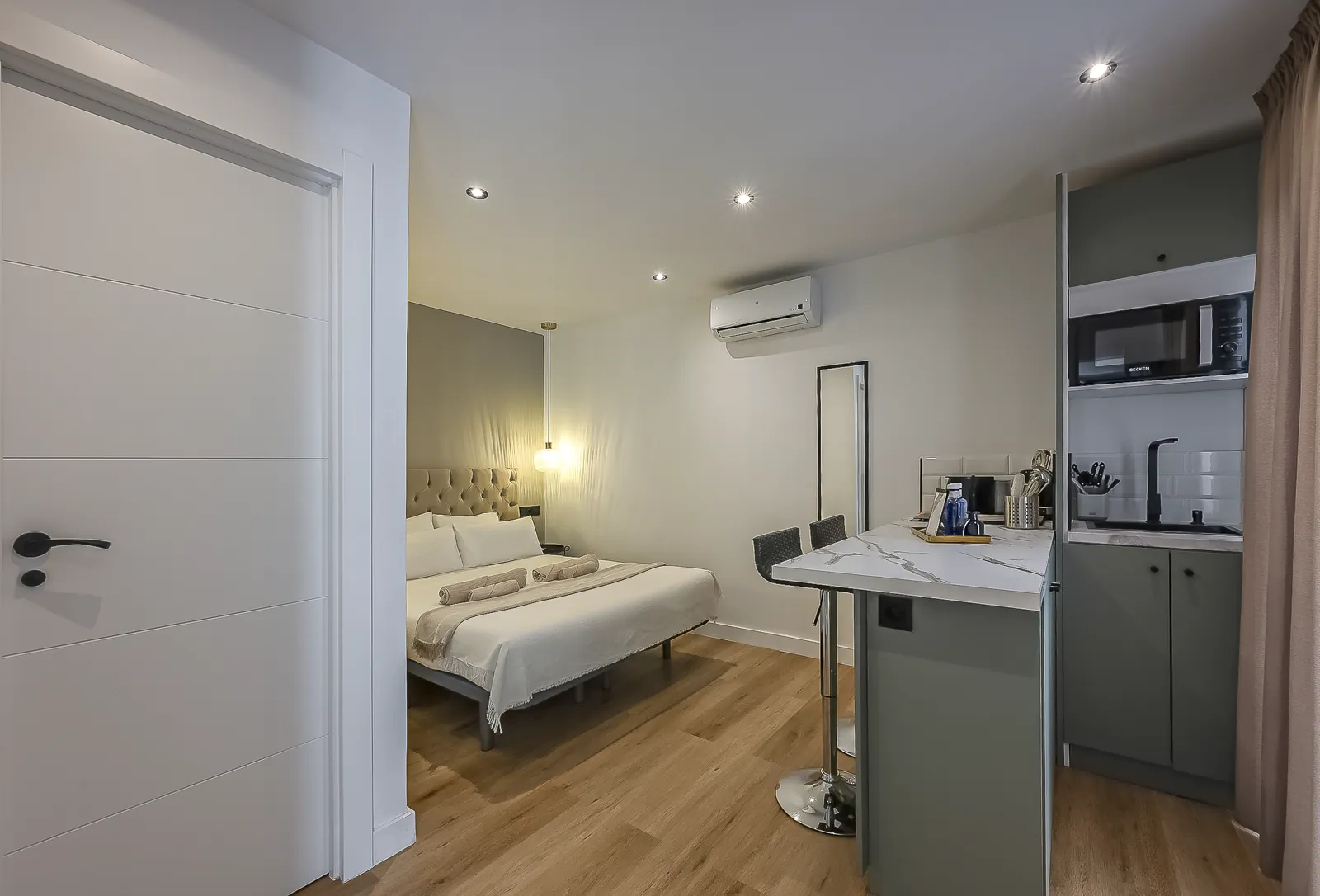 Room 1 from the door: the bed at the far wall and the kitchenette along the right, in oak flooring throughout