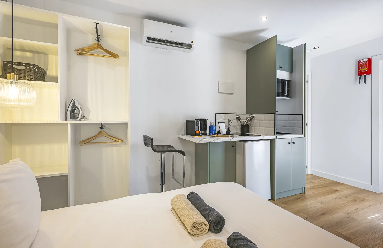 Room 2: the open wardrobe with hangers and an iron, next to the kitchenette and its bar stool
