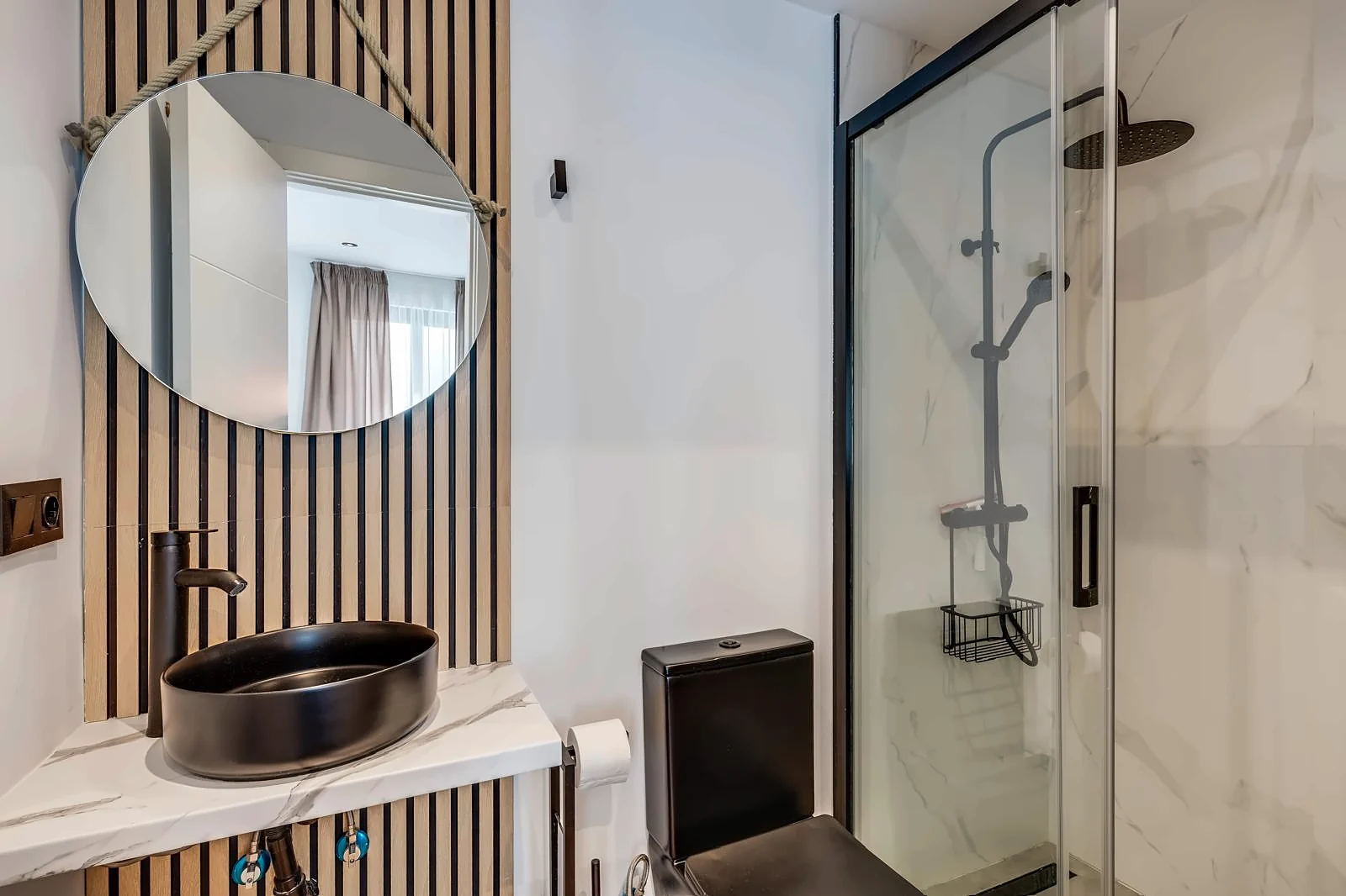 Room 3: a black basin on marble against oak slats, under a round mirror hung on rope, beside the glass shower