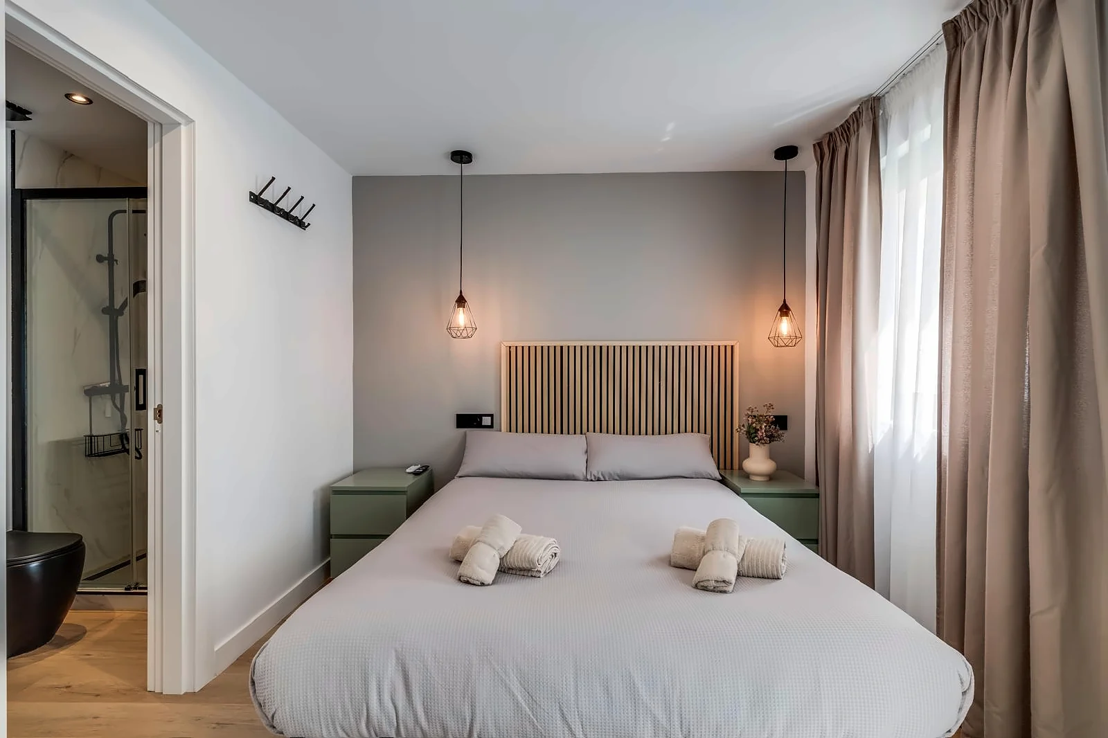Room 3 from the foot of the bed: the oak slat headboard, a wire pendant either side, and the shower room through the open door