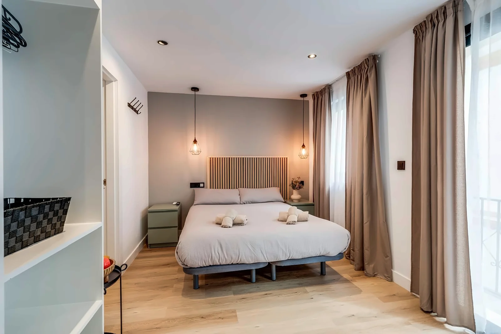 Room 3 from the shelving: the bed between sage green bedside tables, and the windows in linen curtains along the right