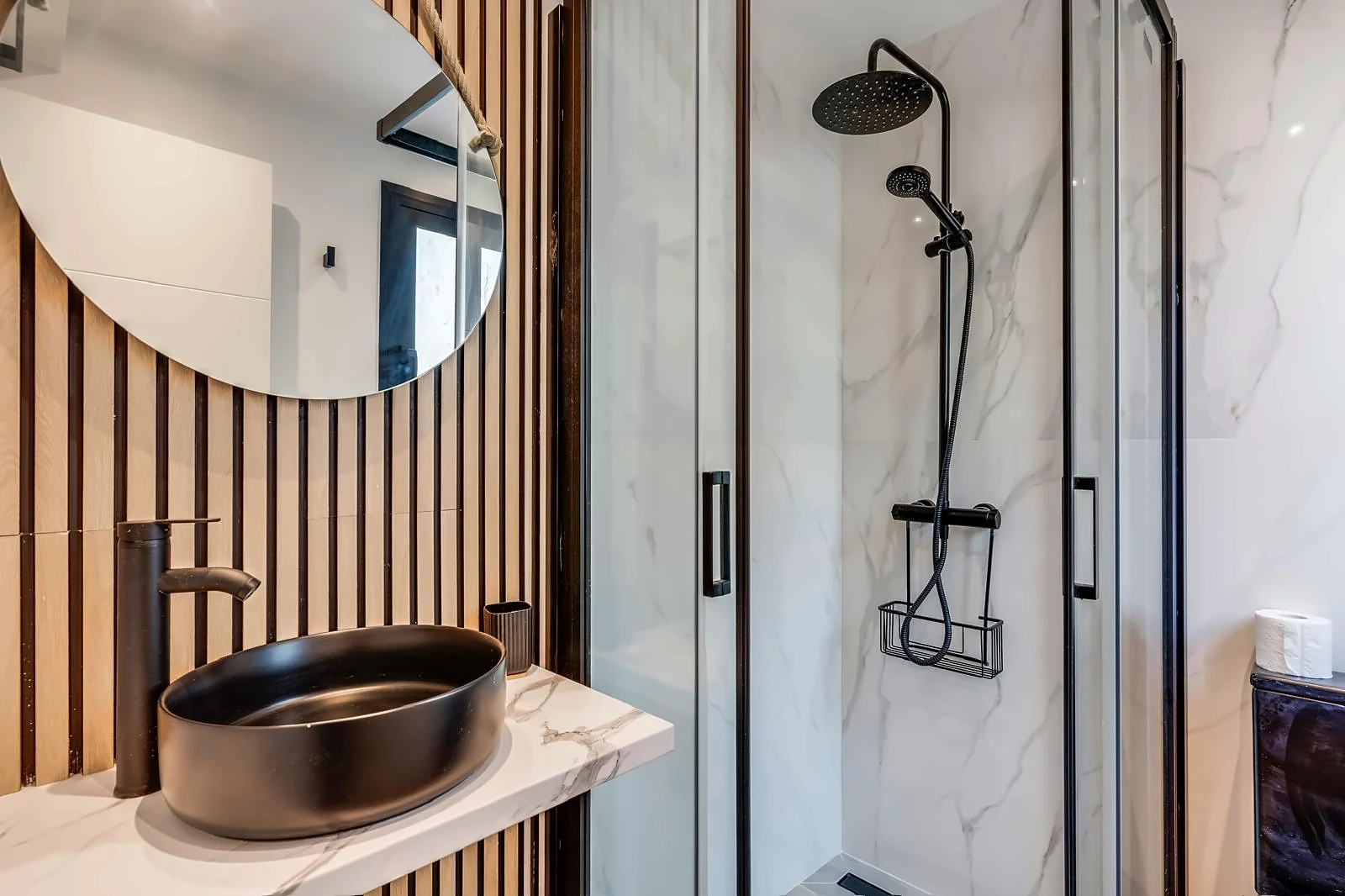 The Micro Suite shower room: marble tile, black framed glass and a black basin under a round mirror