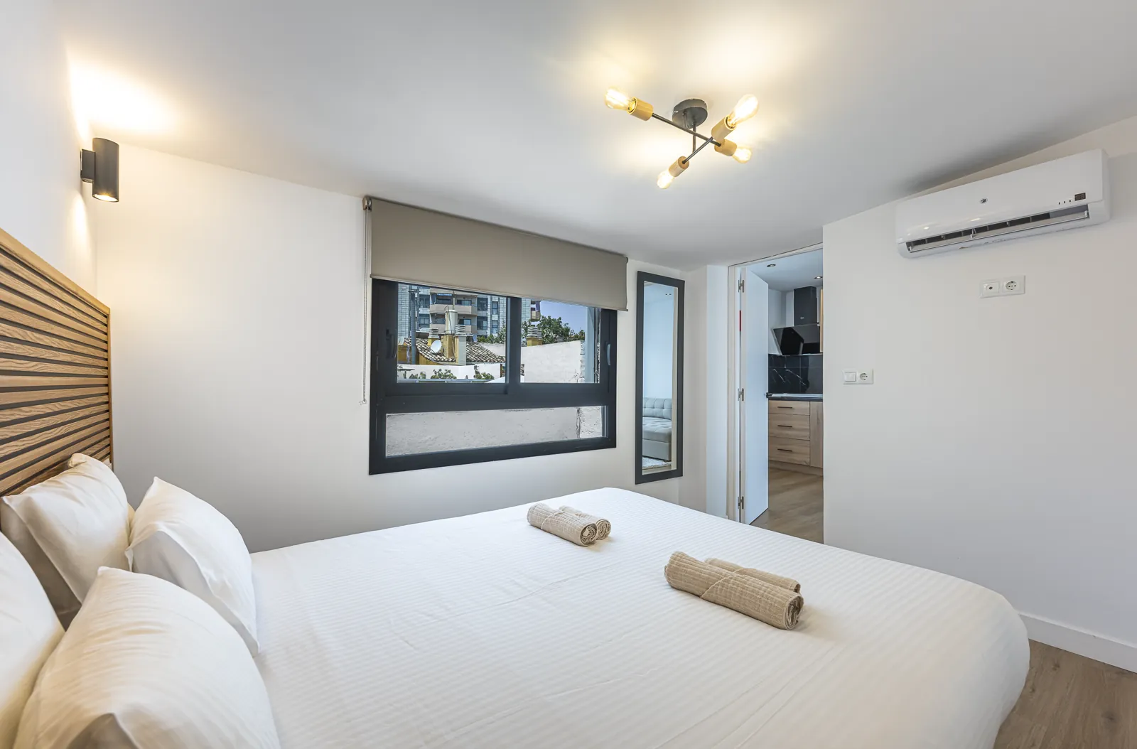 The One-Bedroom Suite bedroom: a wide bed against an oak slat headboard under a brass ceiling light
