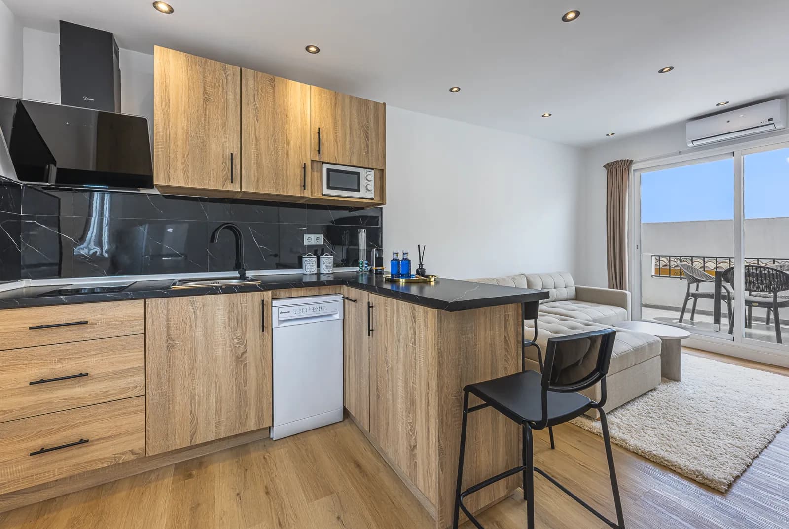 The One-Bedroom Suite kitchen: oak cabinets, a dishwasher and a black stone counter, with the terrace doors beyond