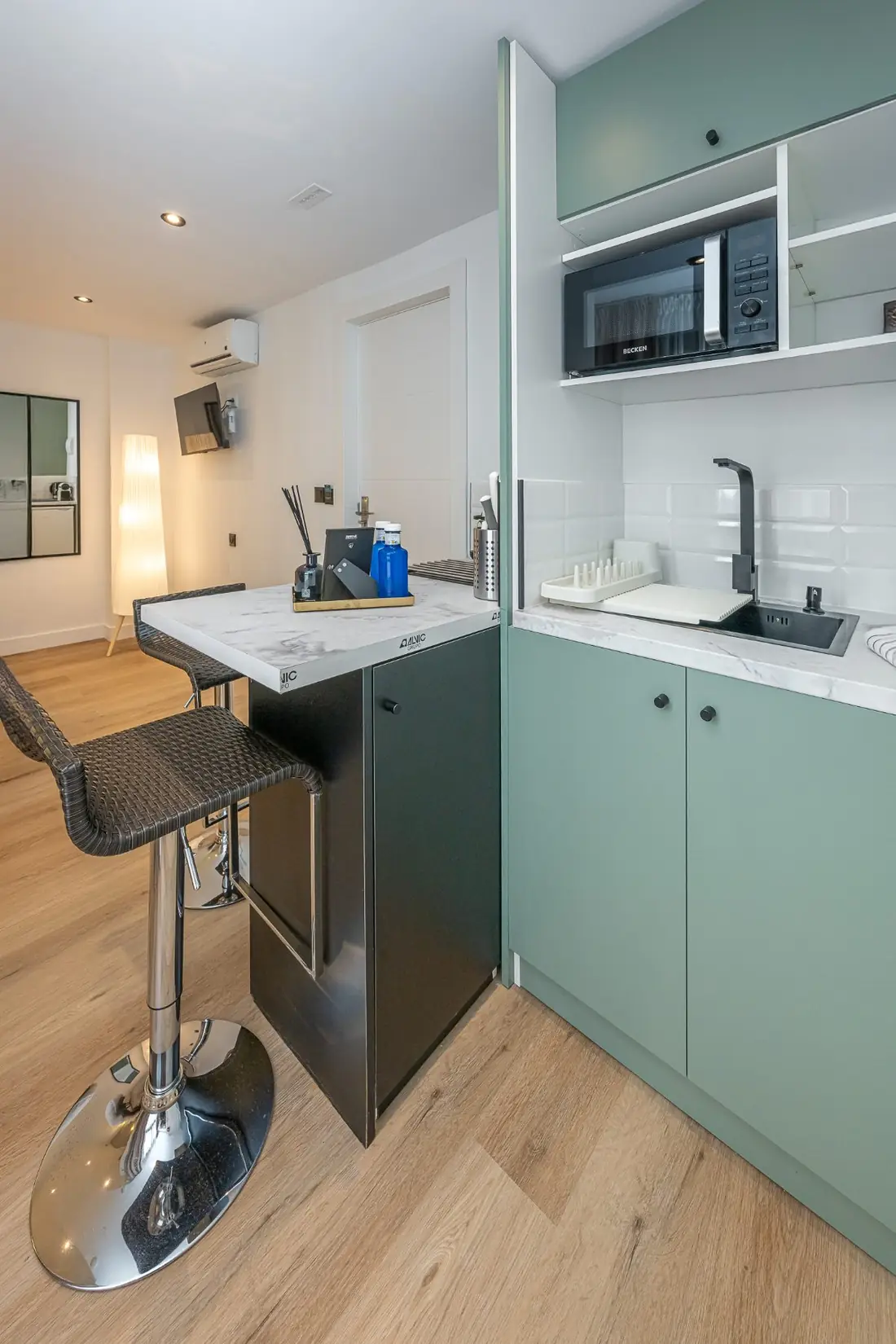 The kitchenette in sage green, with a microwave, a marble bar and a stool