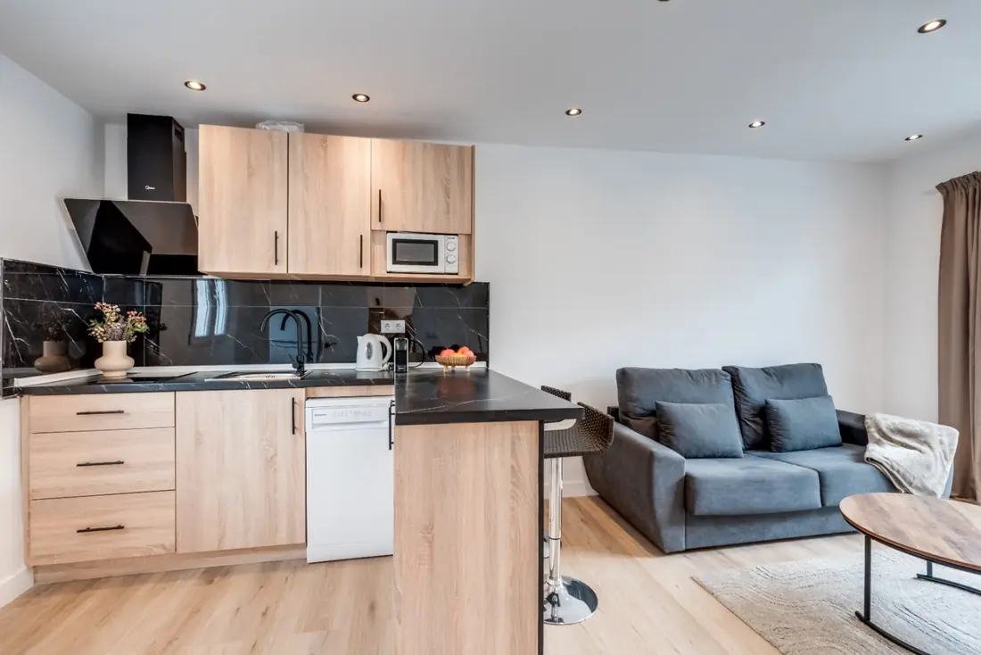 The One-Bedroom Suite: an oak kitchen with a black stone worktop opening onto a sitting room with a grey sofa